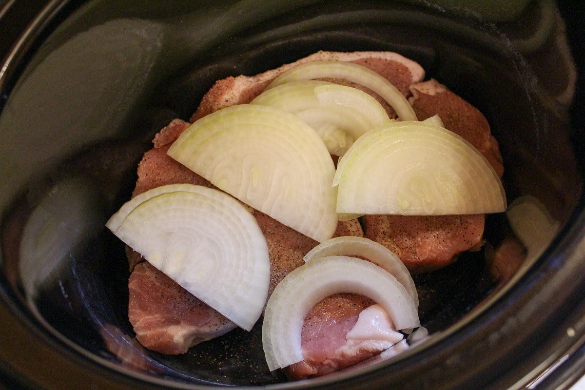 uncooked pork in a slow cooker with raw onions