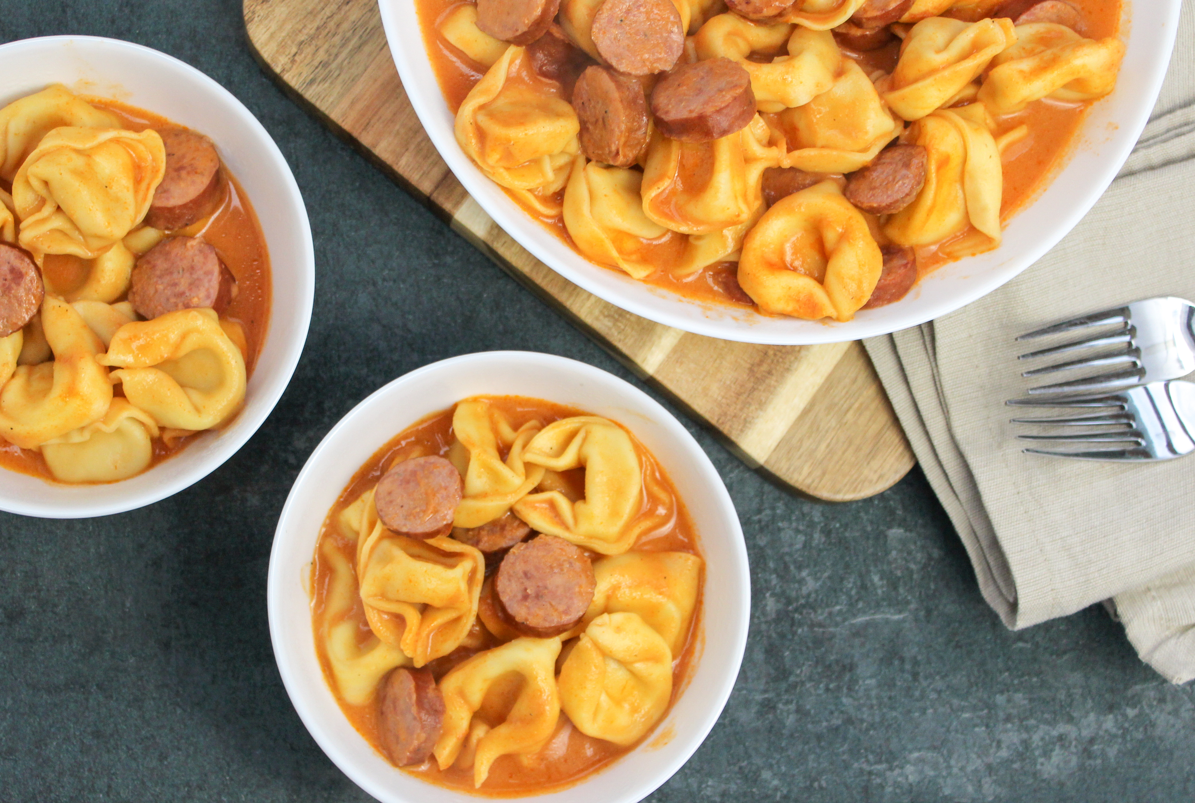 Tortellini and sliced smoked sausage in a whie bowl covered in tomato sauce