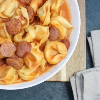 Tortellini and sliced smoked sausage in a whie bowl covered in tomato sauce