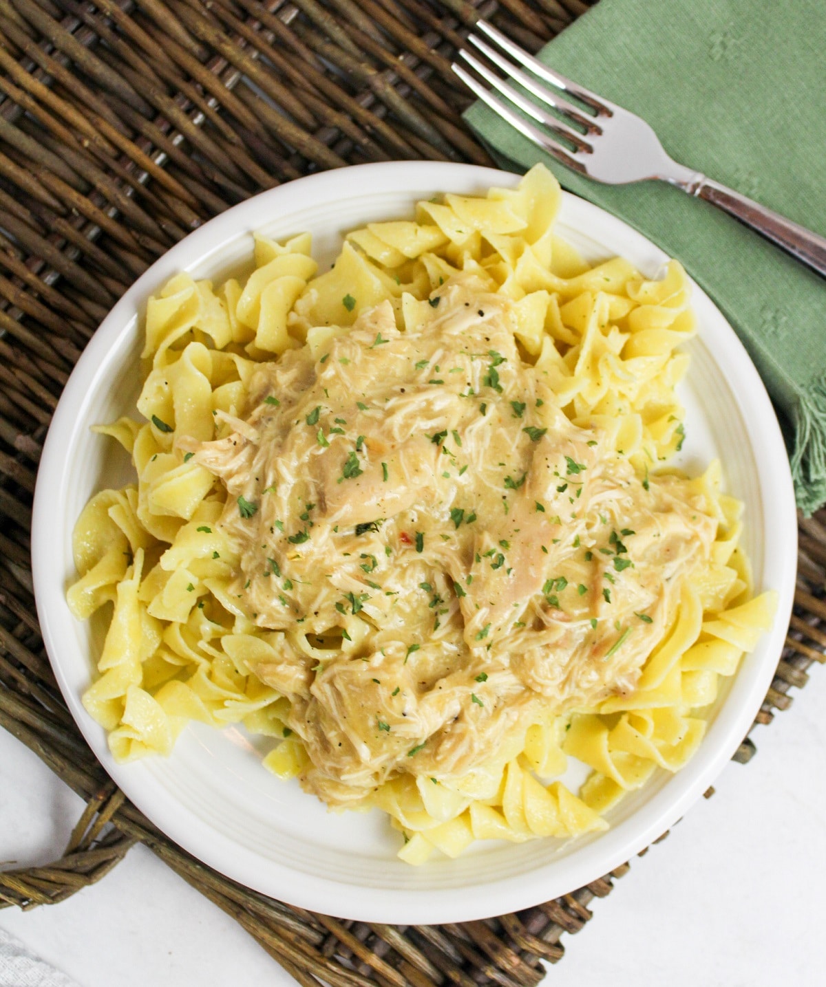 overhead photo slow cooker italian chicken over noodles on a white plate