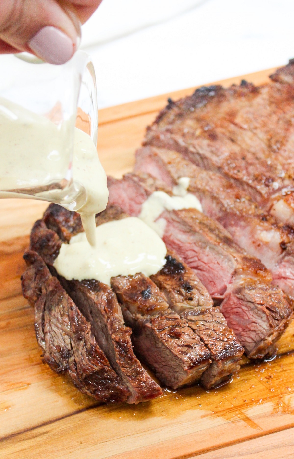Grilled Ribeye with Garlic Blue Cheese Mustard Sauce on a cutting board and sliced with sauce on top