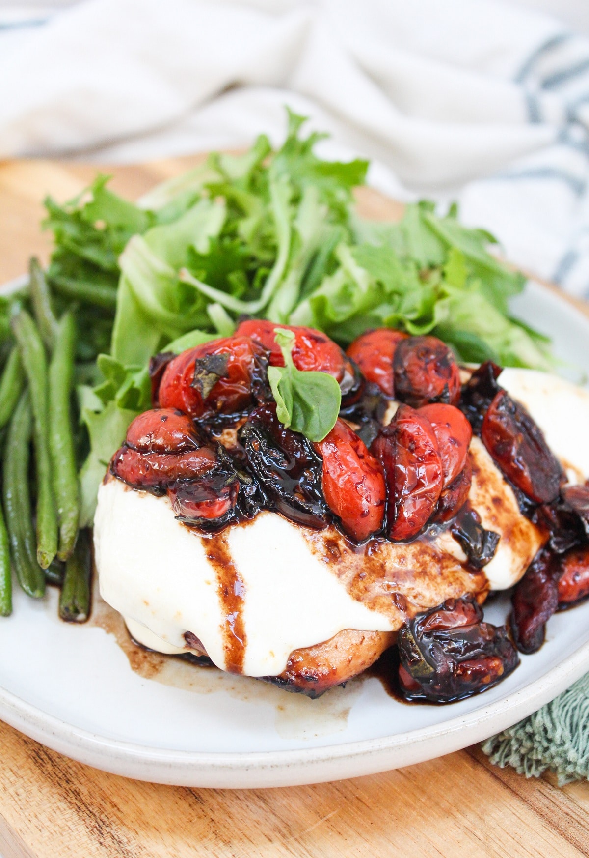 grilled caprese chicken plated with green beans and a salad.