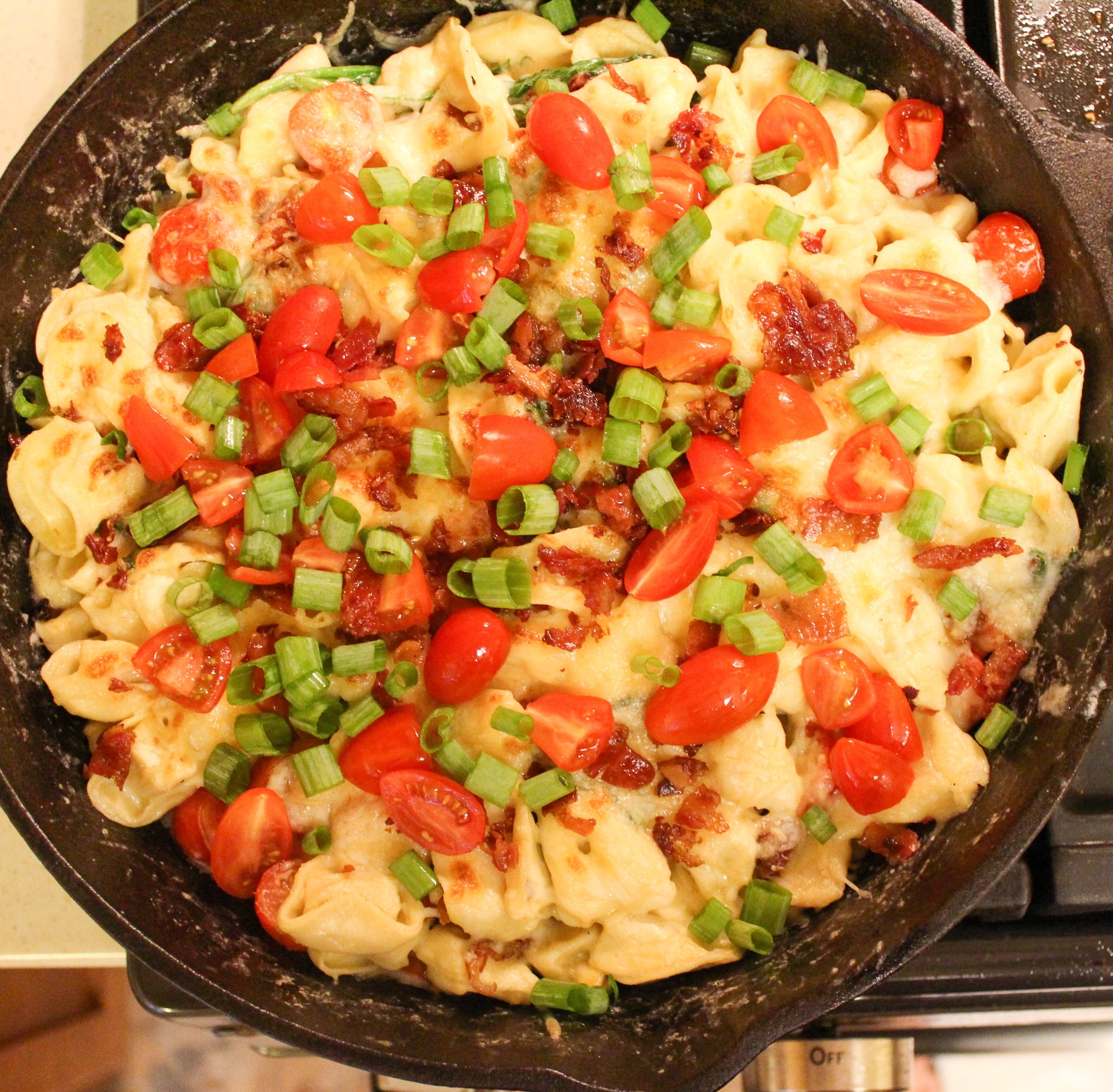 pasta in skillet topped with bacon and tomato and onion