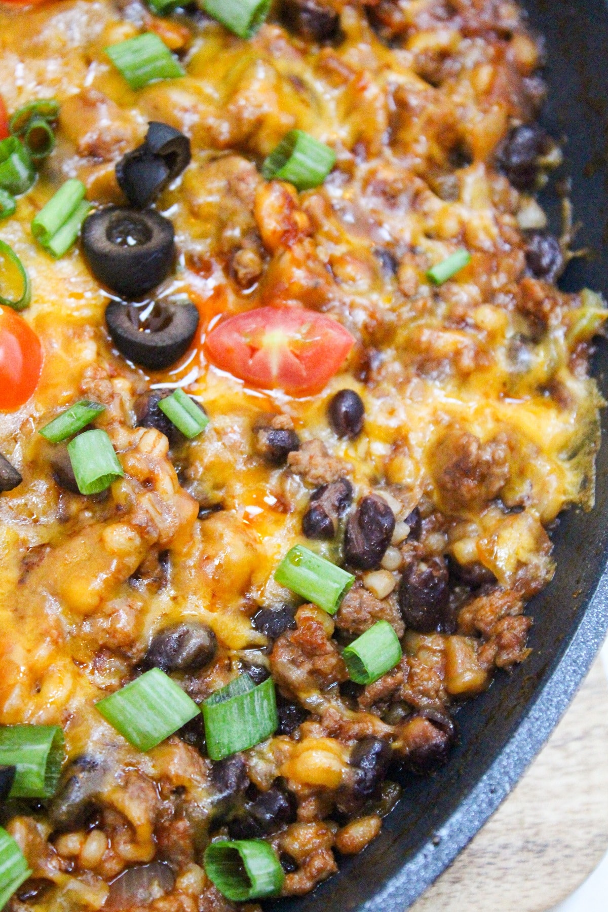 Cheesy Taco Barley Skillet cooked in a pan topped with cheese, black olives, tomatoes, and green onion.