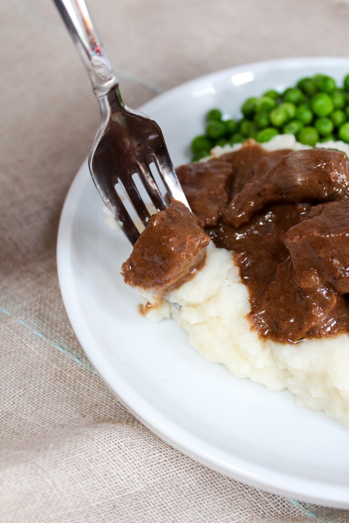 no peek beef tips on a plate with mashed potatoes and peas on a fork