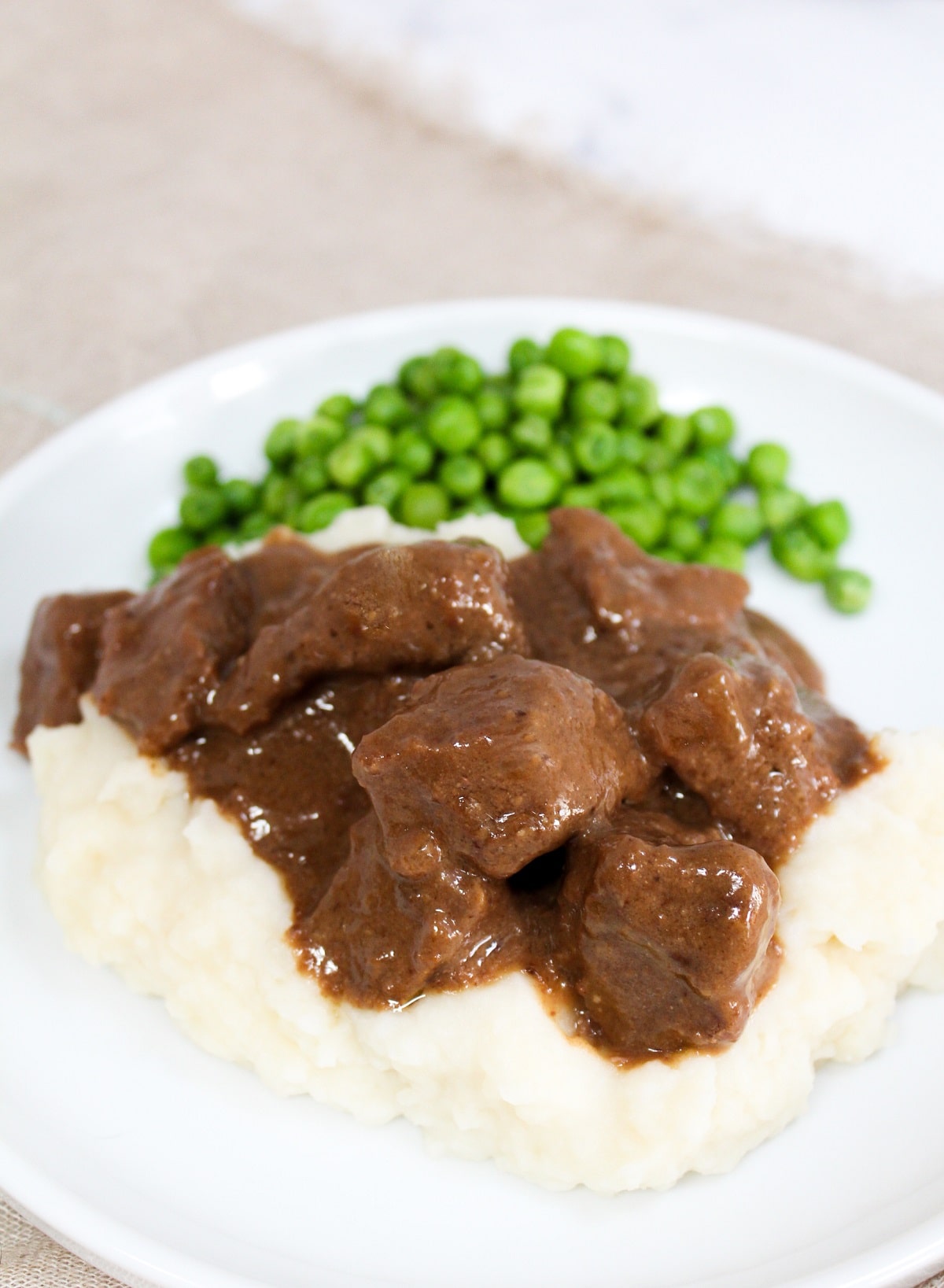 no peek beef tips on a plate with mashed potatoes and peas