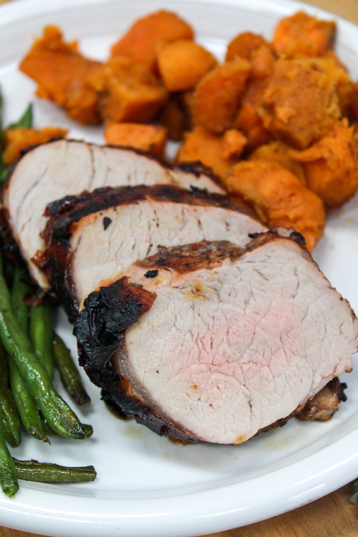 Grilled Honey Balsamic Pork Tenderloin grilled and sliced on a plate with sweet potatoes.