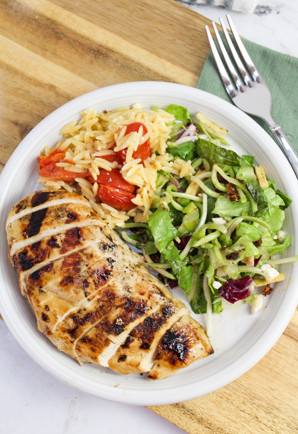 sliced grilled greek chicken on a plate with salad and rice.