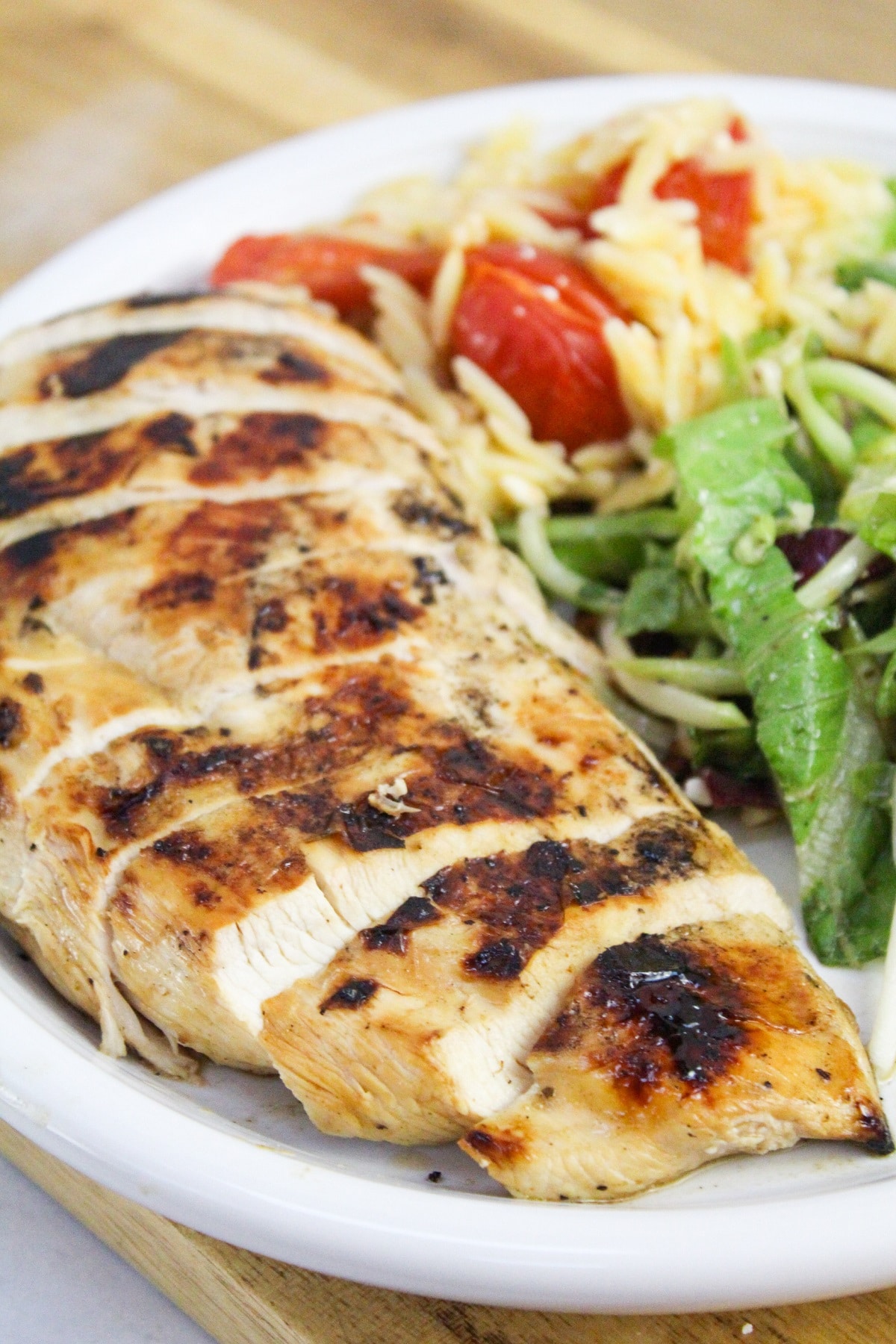 sliced grilled greek chicken on a plate with salad and rice.