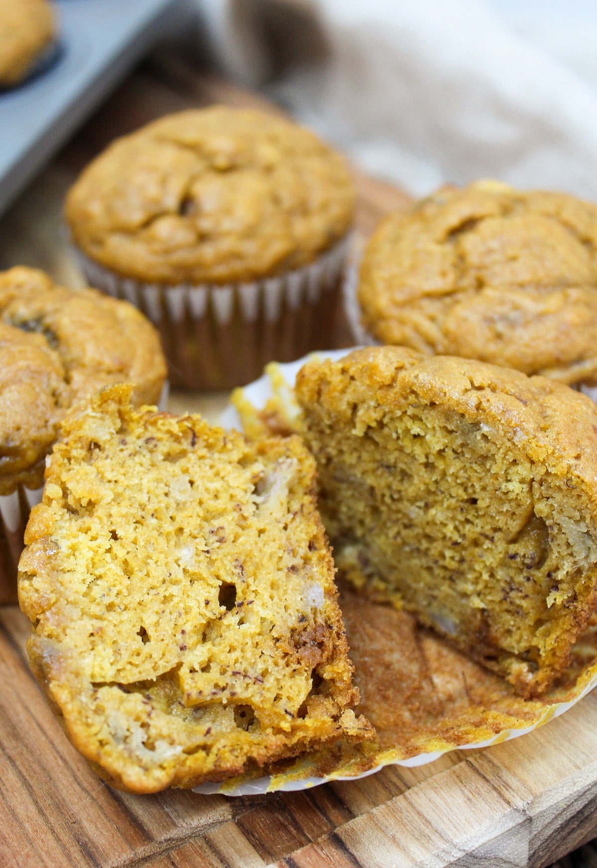 baked muffins on a cutting board with wrappers. The muffin is unwrapped and cut in half.