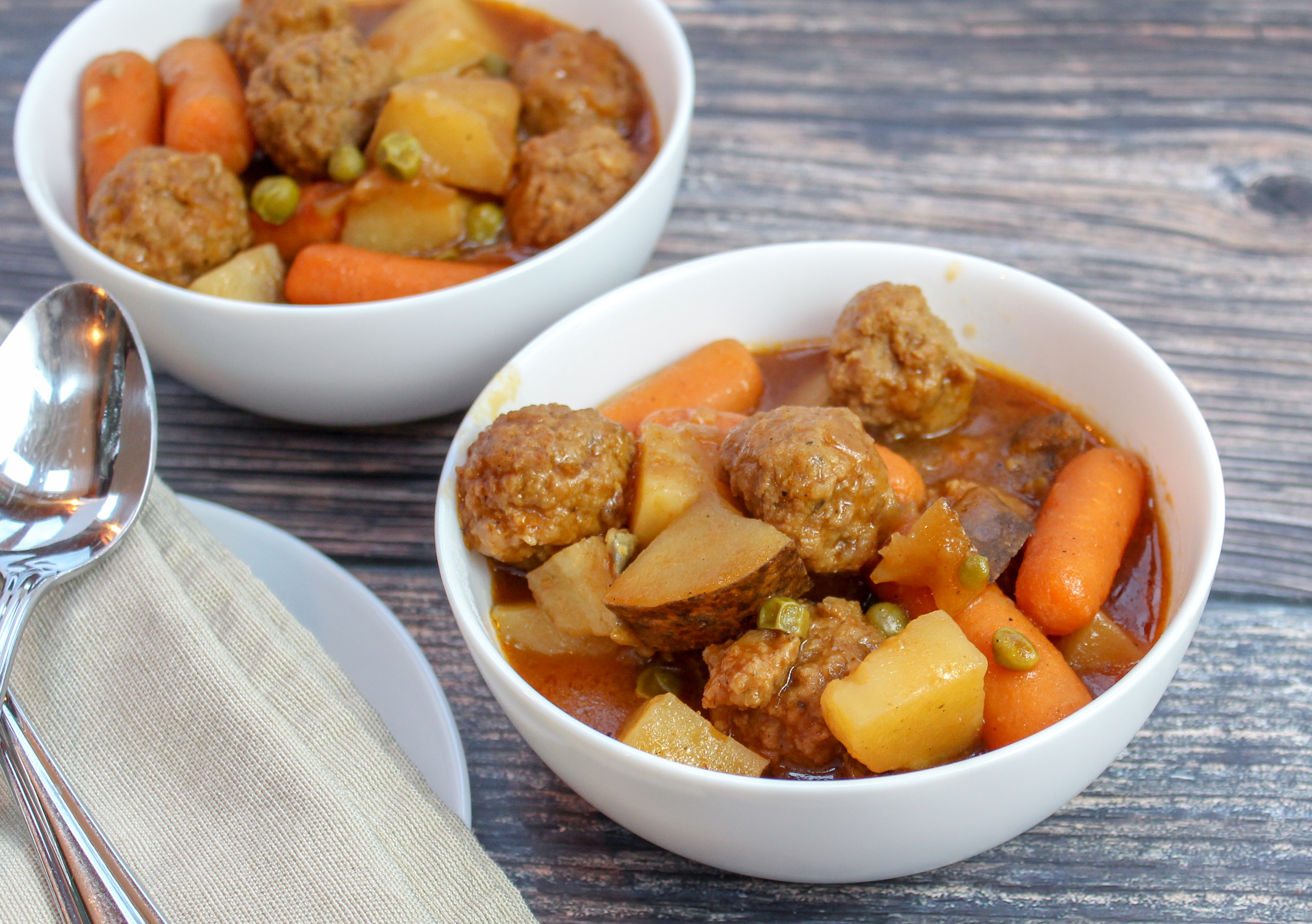 White bowl filled with meatballs, carrots, celery, potatoes and peas