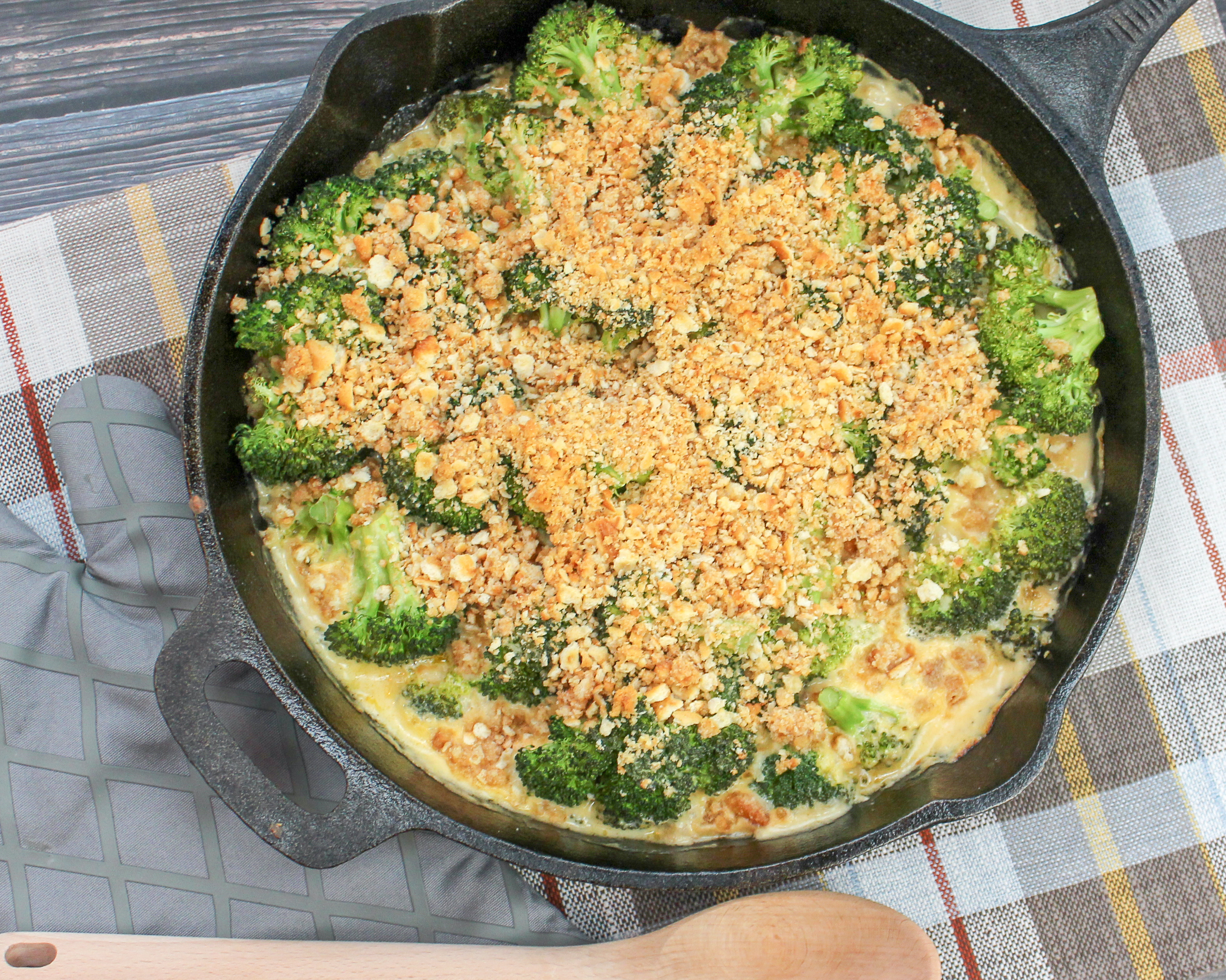 Broccoli florets covered in cheese sauce and topped with crushed crackers. Served in a round black baking pan.