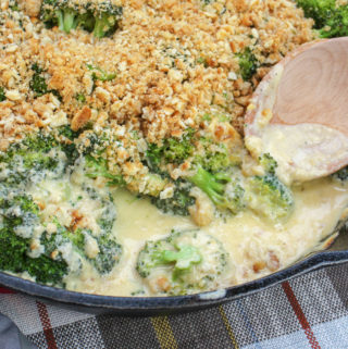 Broccoli florets covered in cheese sauce and topped with crushed crackers. Served in a round black baking pan.