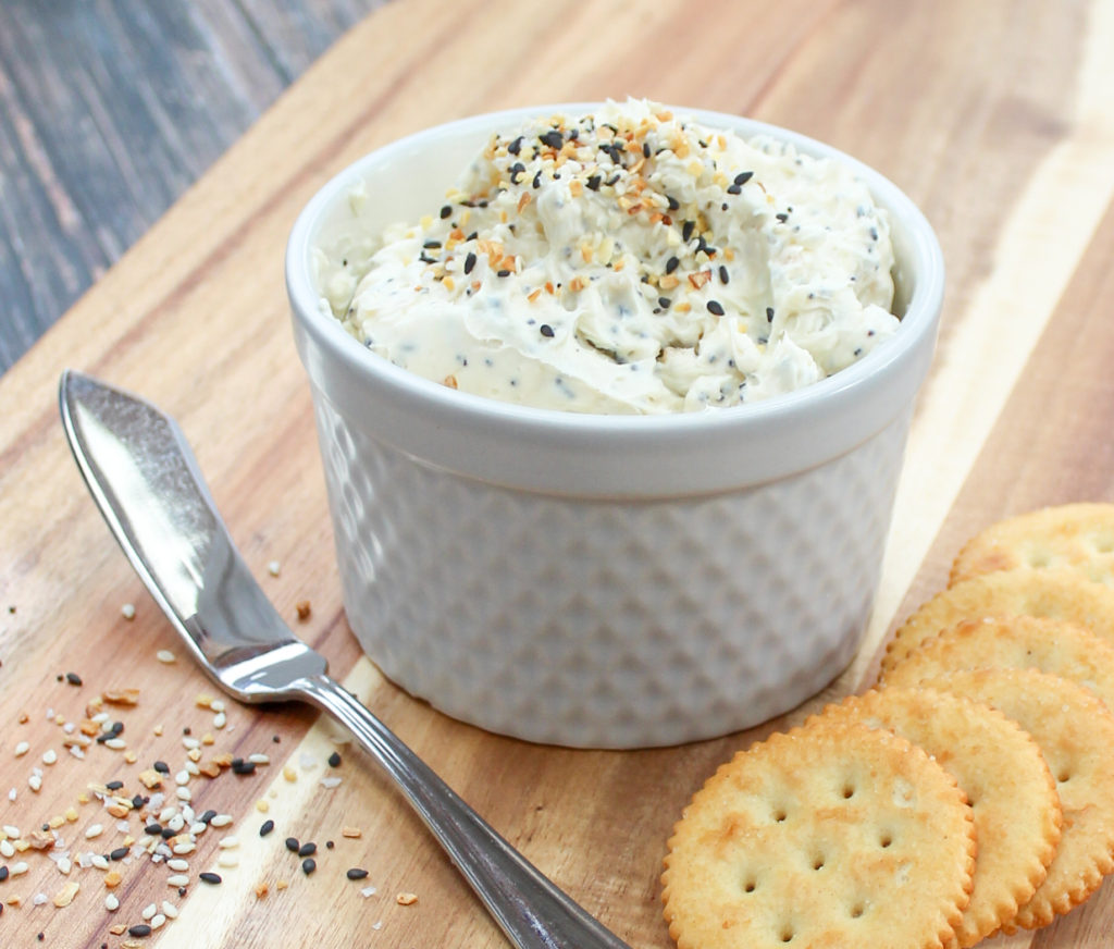 Spread in a white container wth crackers and a spreading knife