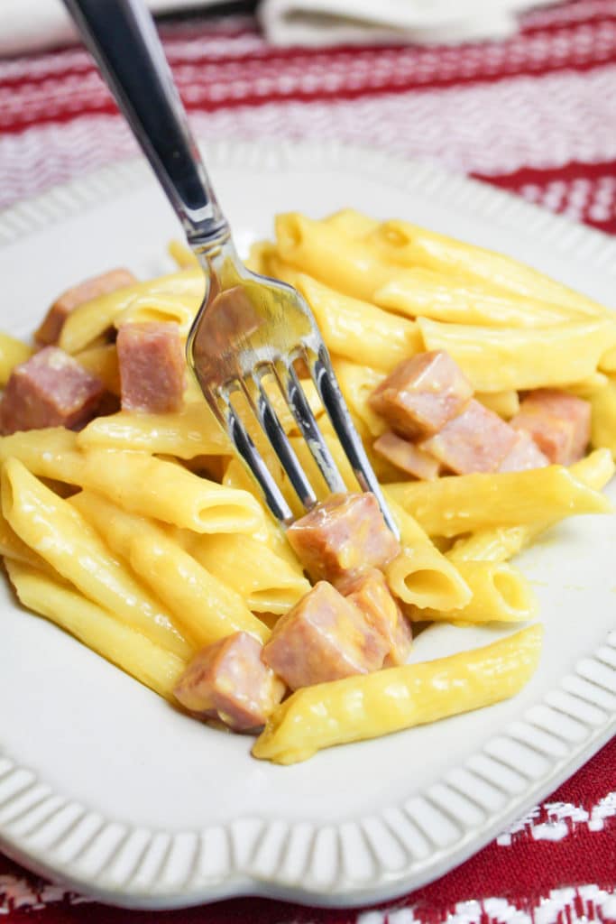 Ham and cheese pasta on a white dinner plate with a fork