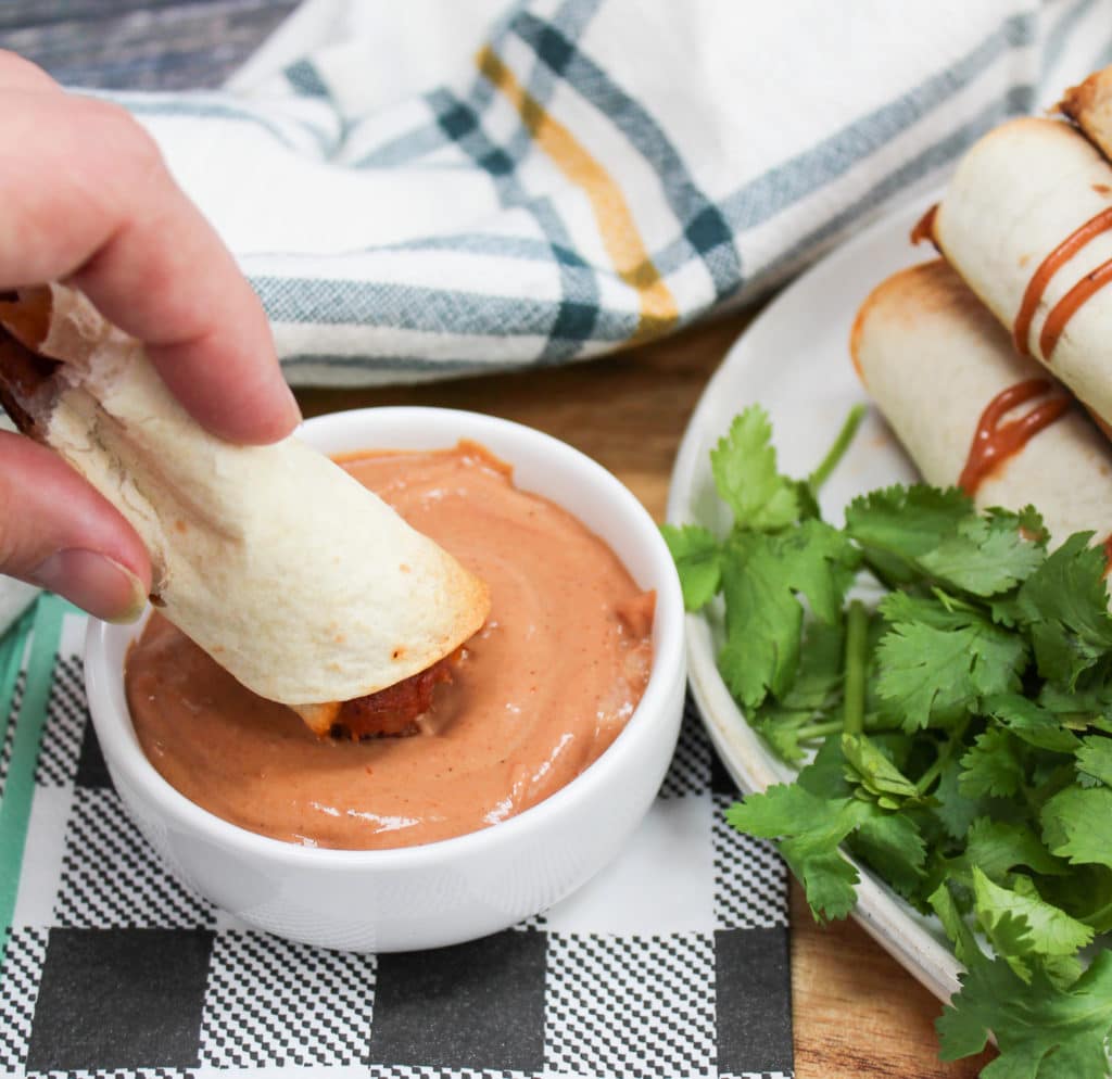 Taquitos in a plate and dipped in sauce