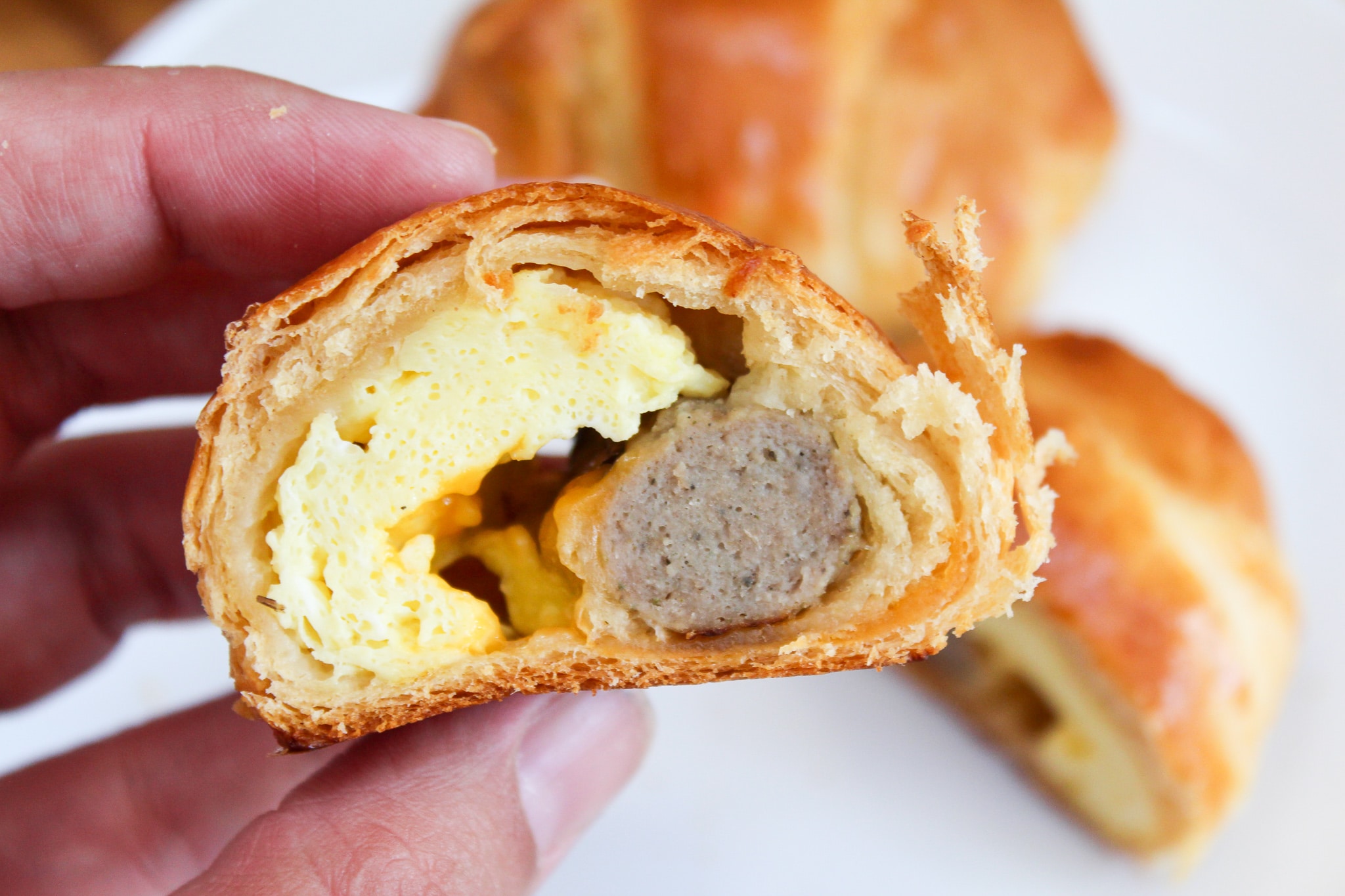 roll-up cut in half to see eggs and sausage and held in hand