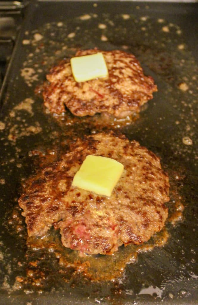 burgers on flat top cooking with butter