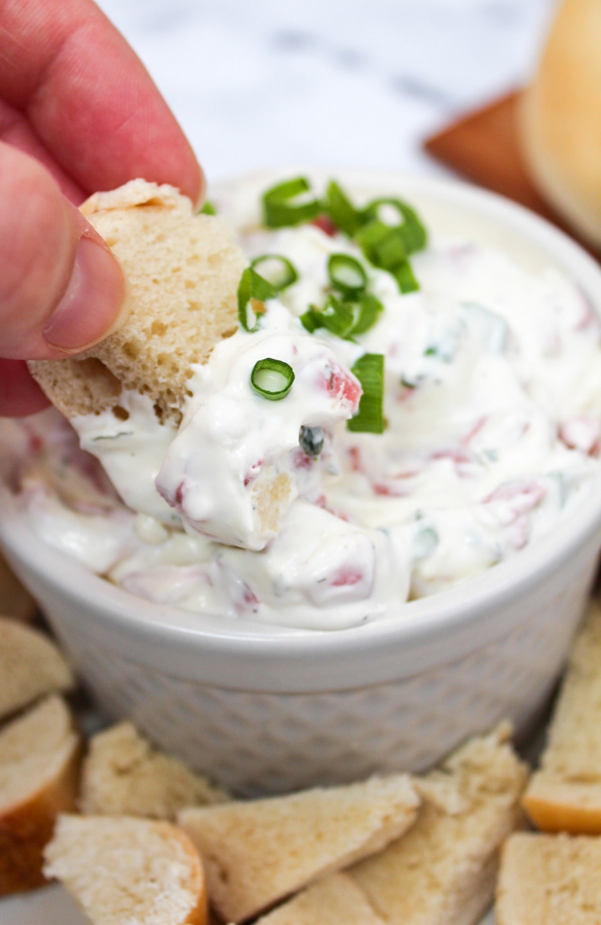 bagel dip in a white dish with bagel piece held in hand and dipped