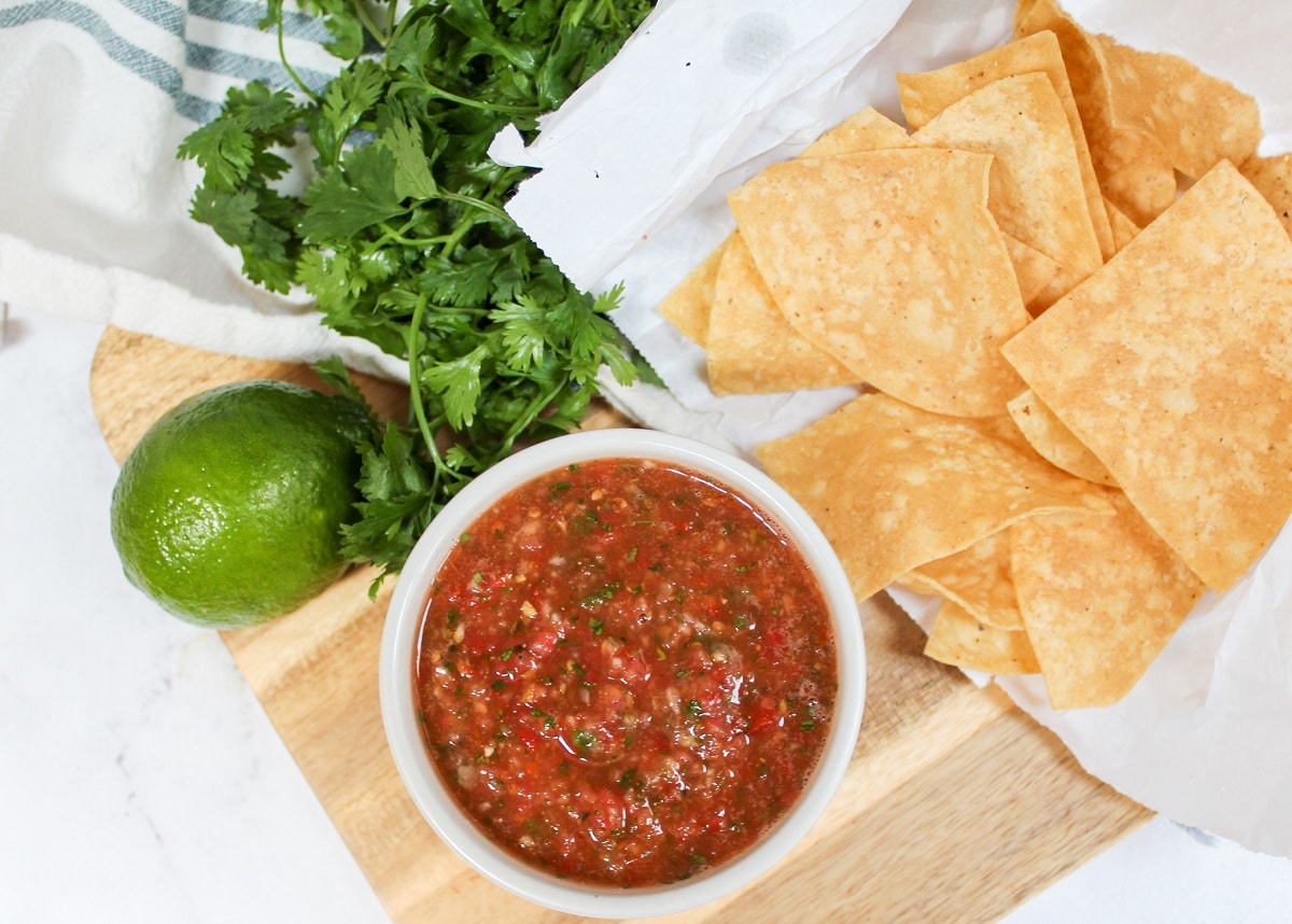 blender salsa in a white bowl with chips, limes, and cilantro on the side