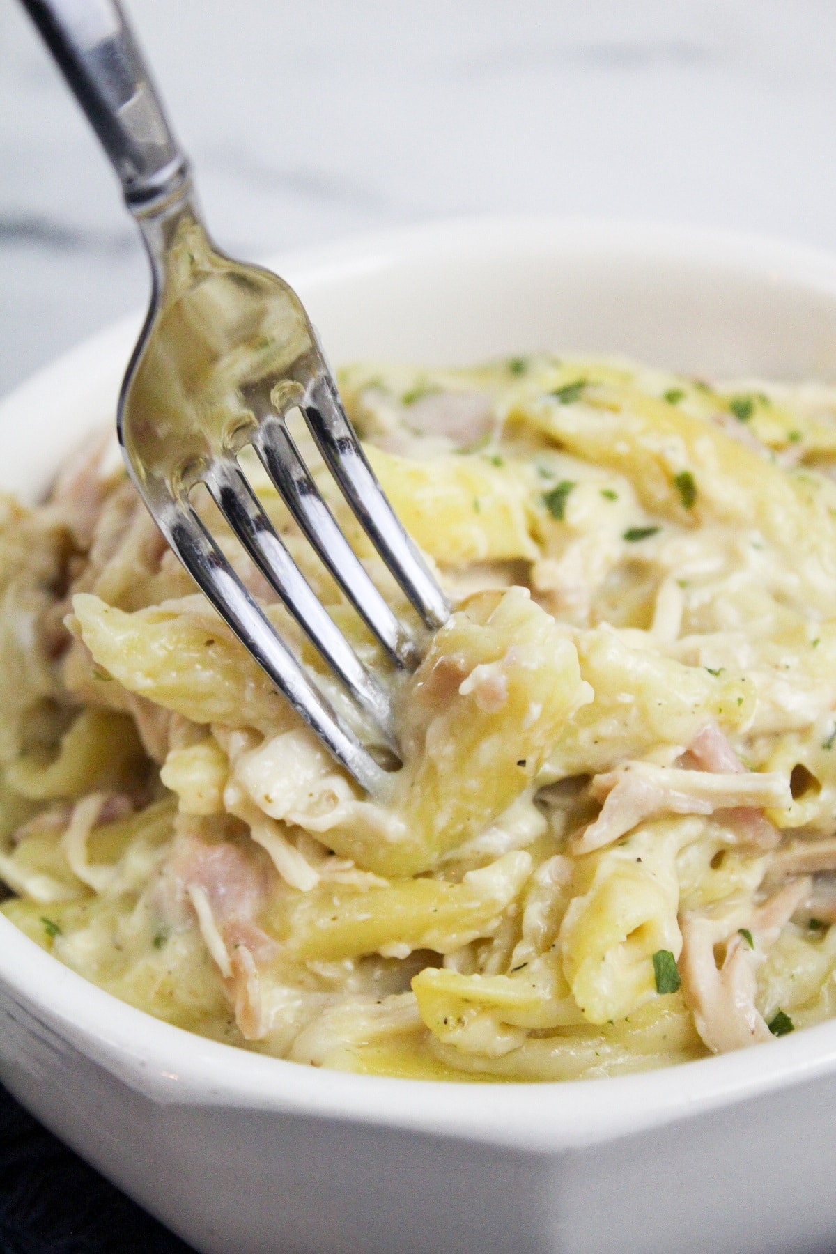 chicken cordon bleu pasta with a fork in a white bowl
