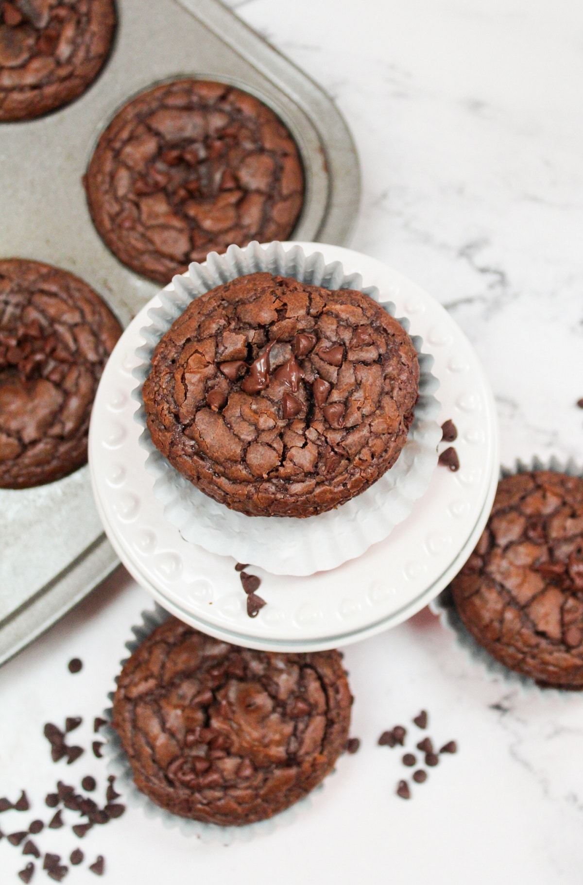 brownie muffins on a white plate with other in a muffin tin to the side