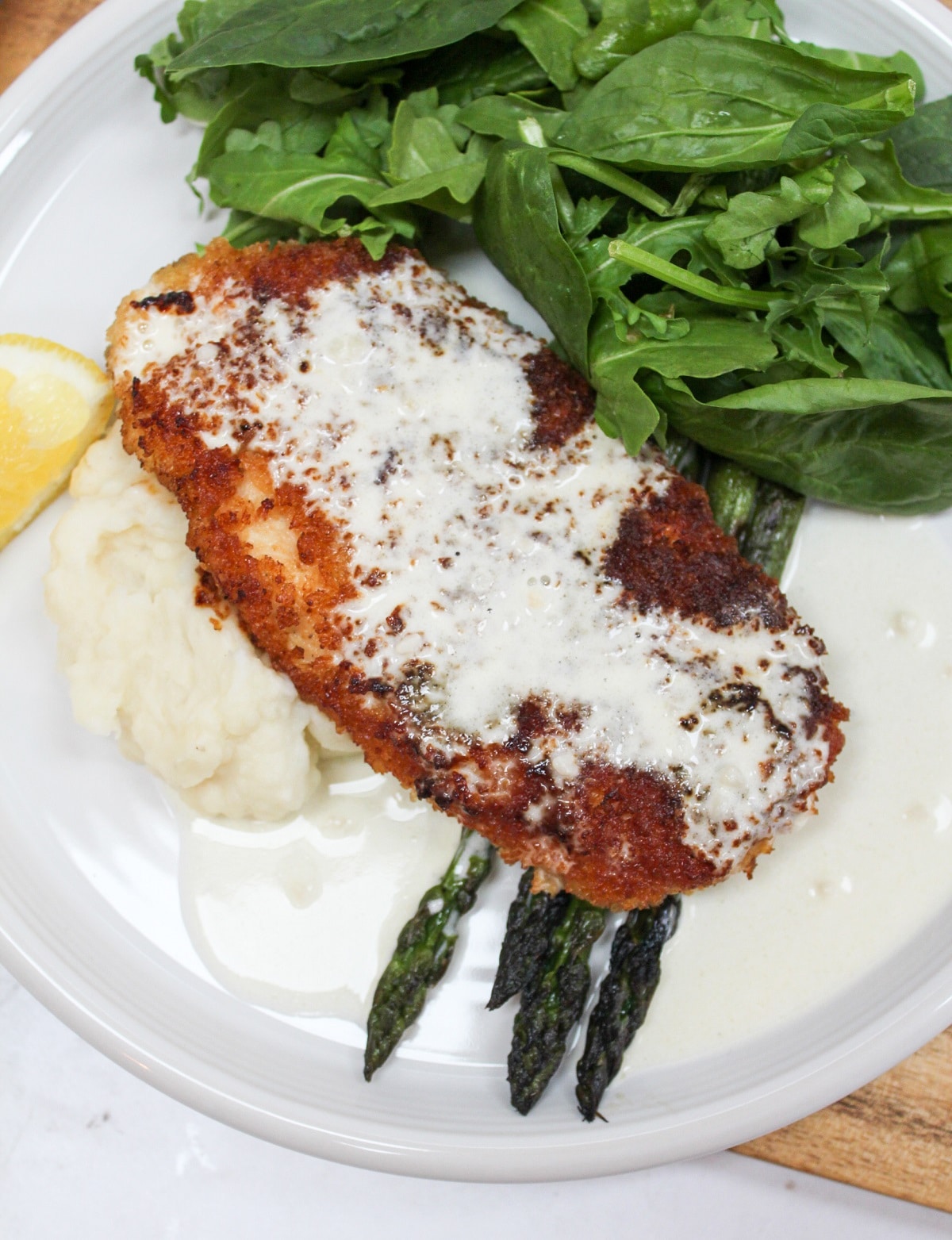 chicken costoletta on a plate with lemon sauce and asparagus.