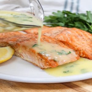 salmon on a white plate with lemons with sauce poured over the top.
