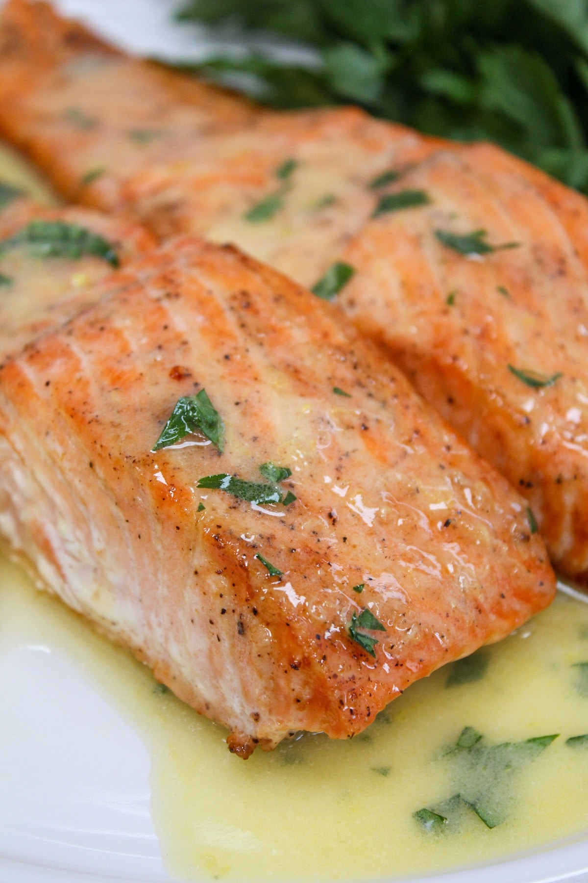 salmon on a white plate with lemons with sauce poured over the top.