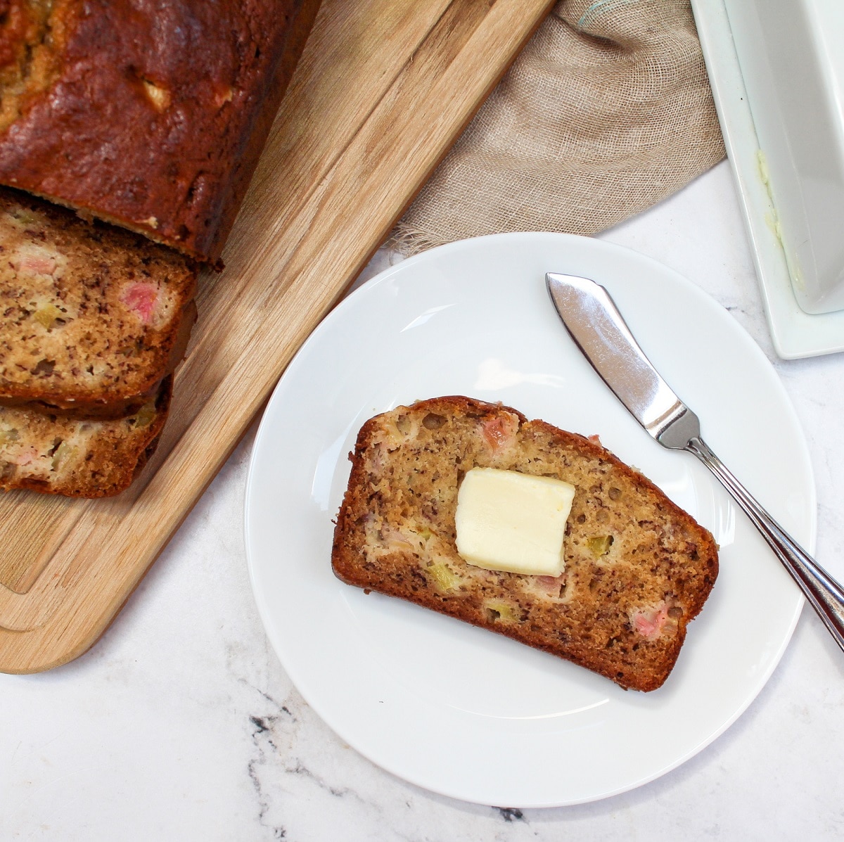 Sliced Rhubarb Banana bread on a white plate with butter.