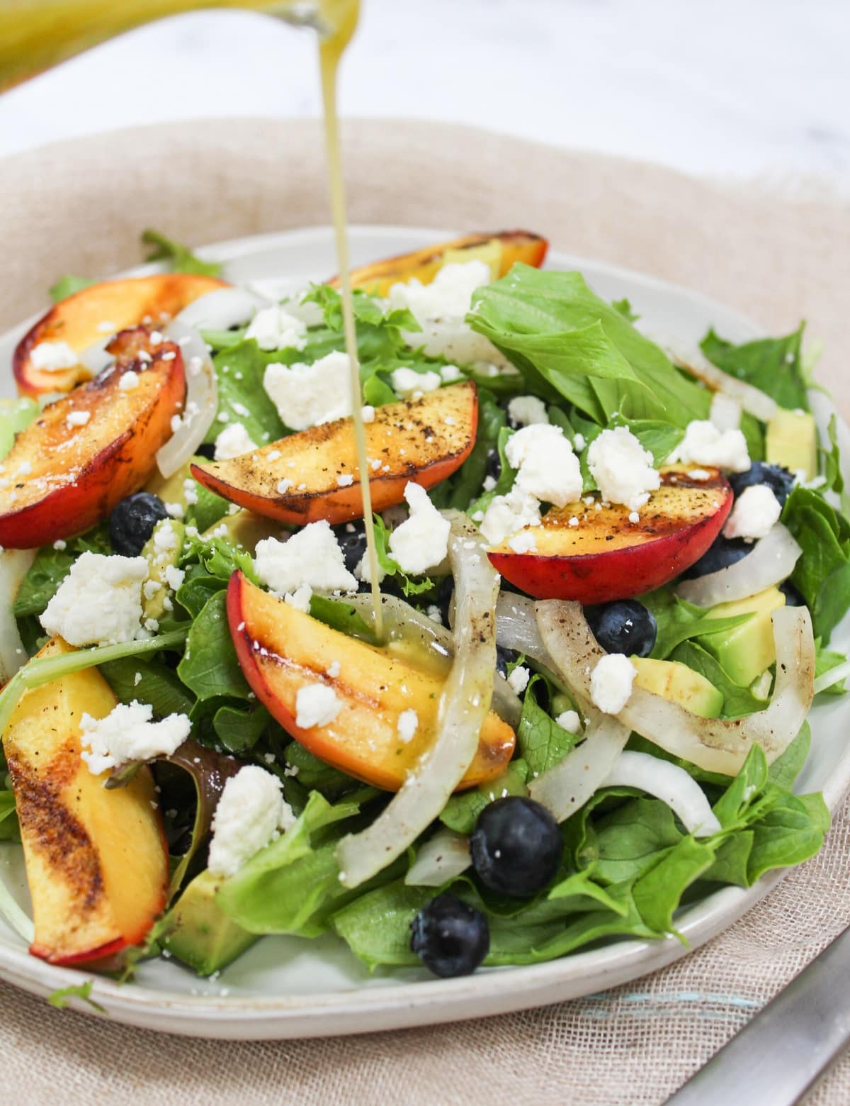 Lettuce topped with sliced onions, grilled peaches, blueberries, and feta with dressing poured on top.