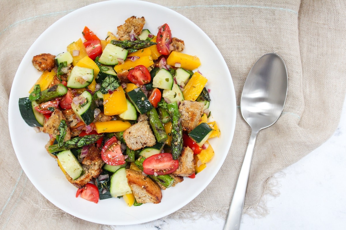 asparagus panzanella salad in a white bowl with serving spoon.