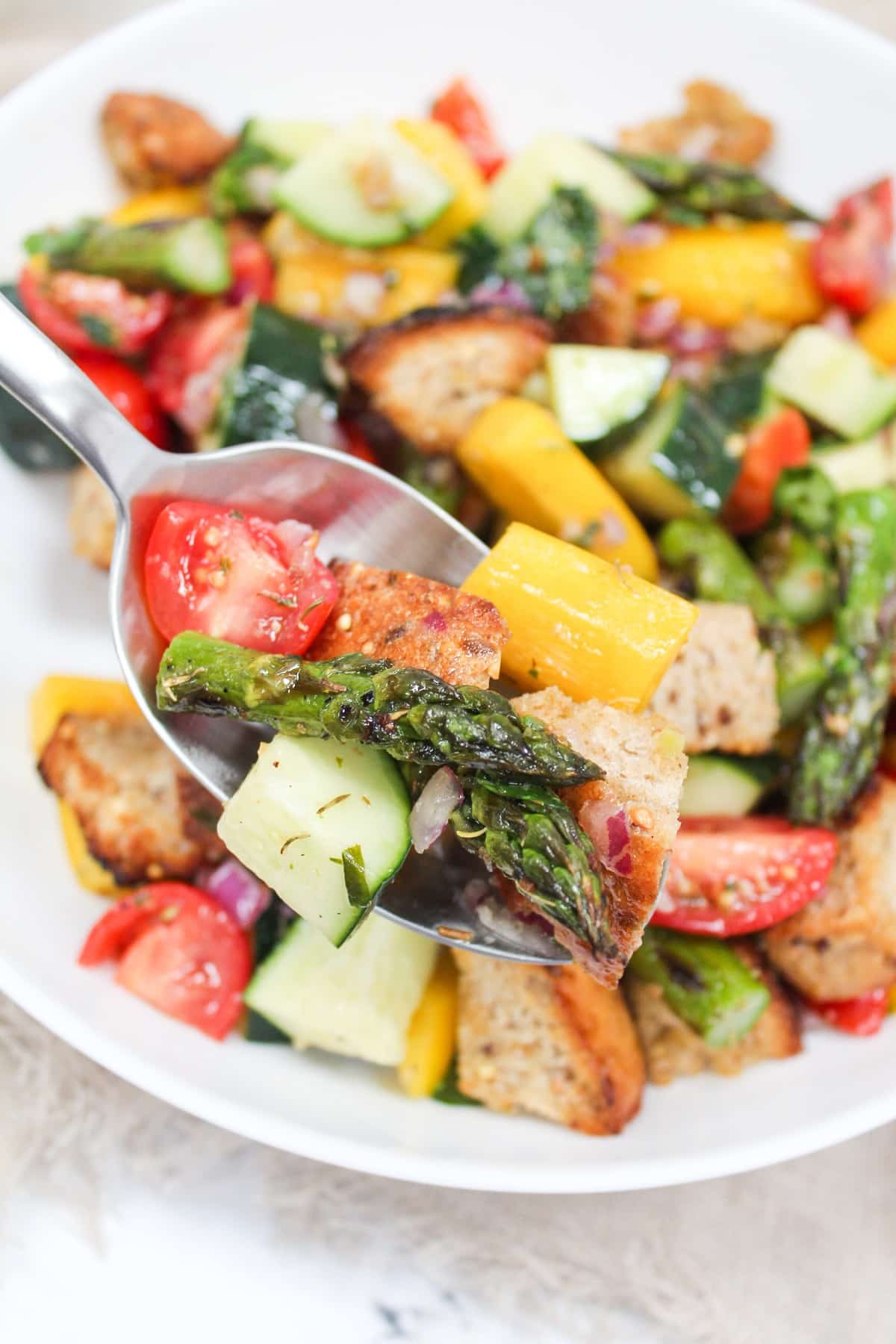 asparagus panzanella salad in a white bowl with serving spoon.