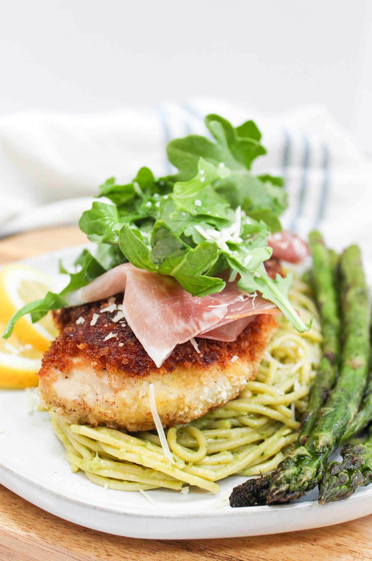 chicken bellagio over pasta topped with arugula and served wit asparagus.