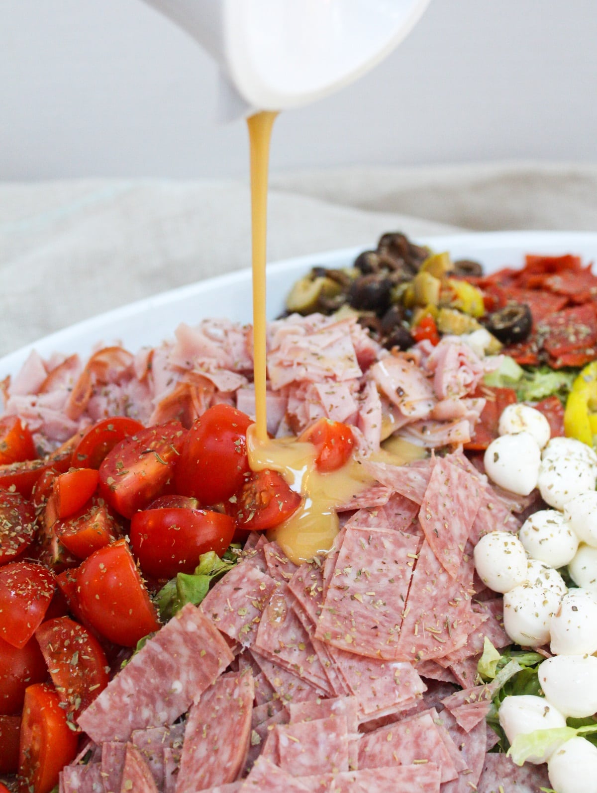 Italian sub salad with tomatoes, pepperoni, ham, olives, and cheese on a plate with ingredients unmixed. The dressing is poured over the salad.