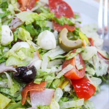 Italian sub salad with tomatoes, pepperoni, ham, olives, and cheese on a plate.