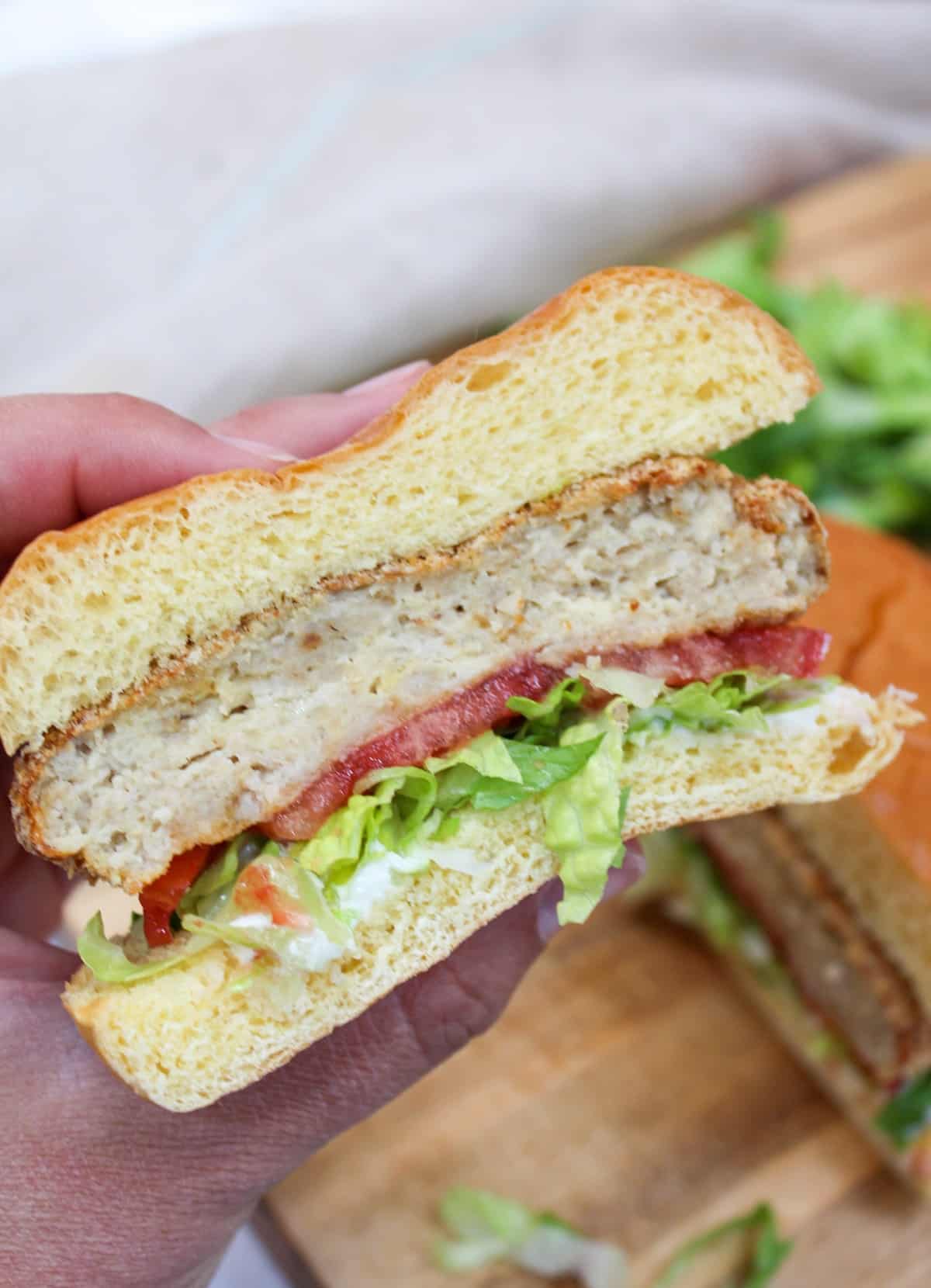 crispy chicken patty on a bun with shredded lettuce and sliced tomato. cut in half and held in hand.