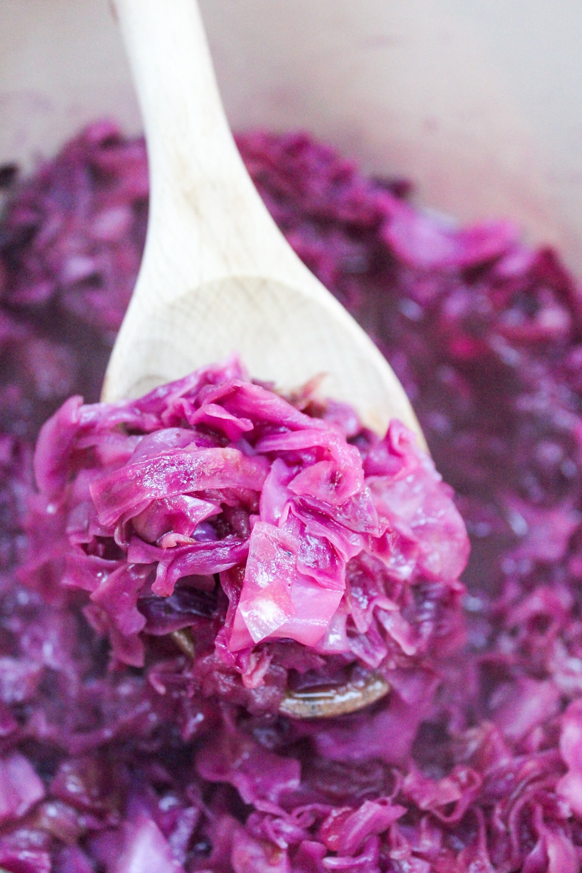 chopped red cabbage and apples in a red pot. Stirred with a wooden spoon.