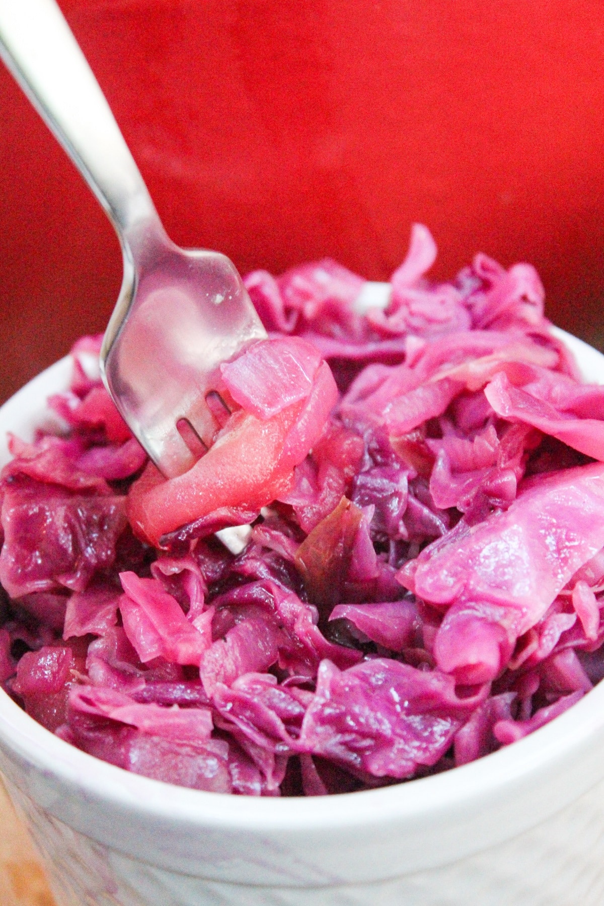 chopped red cabbage and apples in a small white dish with a fork.