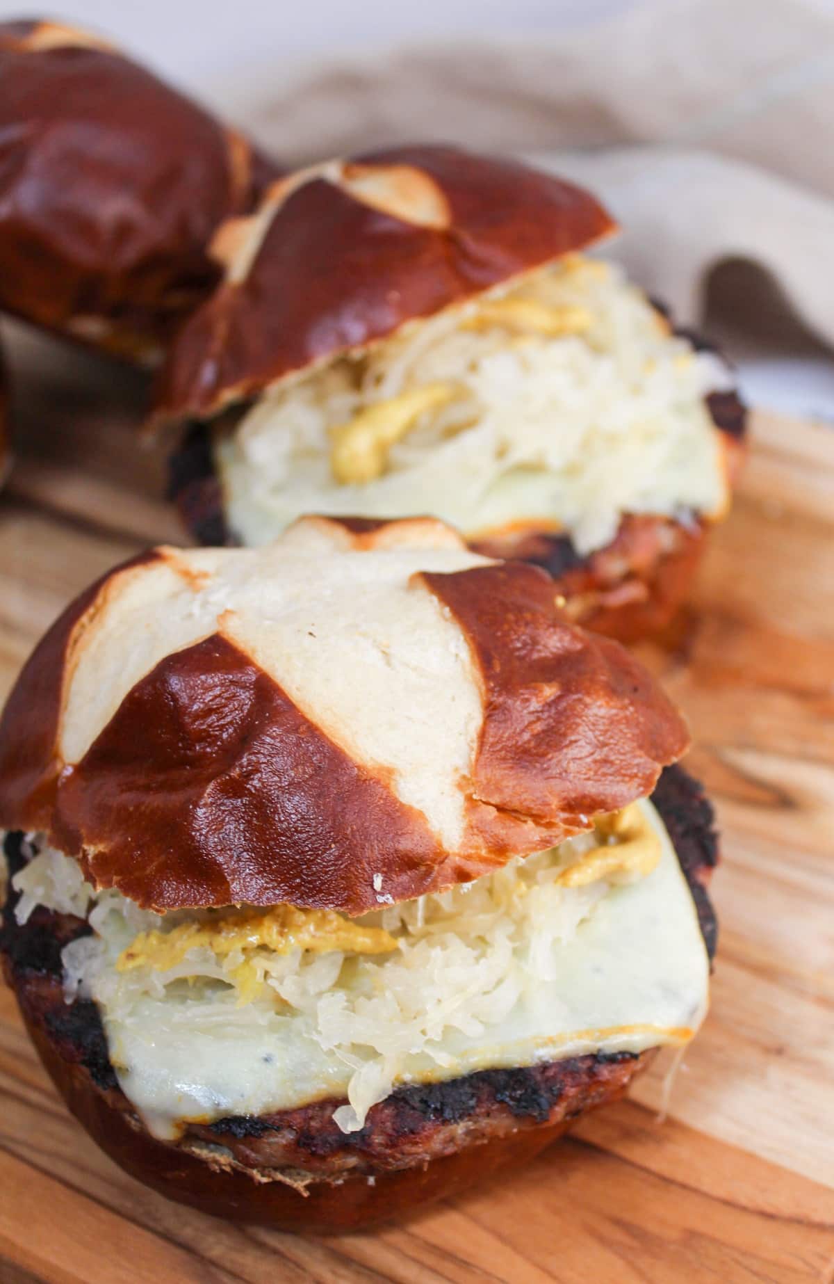 grilled brat pattie on a pretzel roll. The meat is cooked and topped with melted cheese, mustard, and sauerkraut.