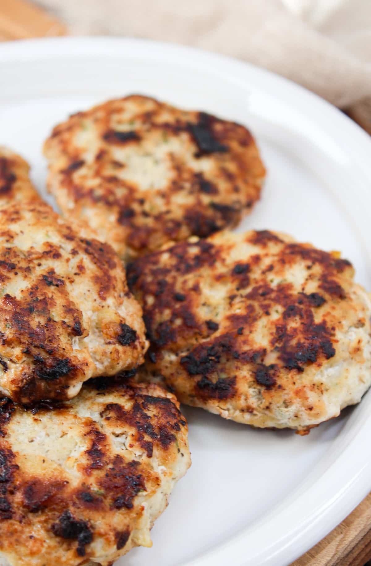 chicken formed into sausage patties. Cooked in a skillet till golden brown and served on a white plate.