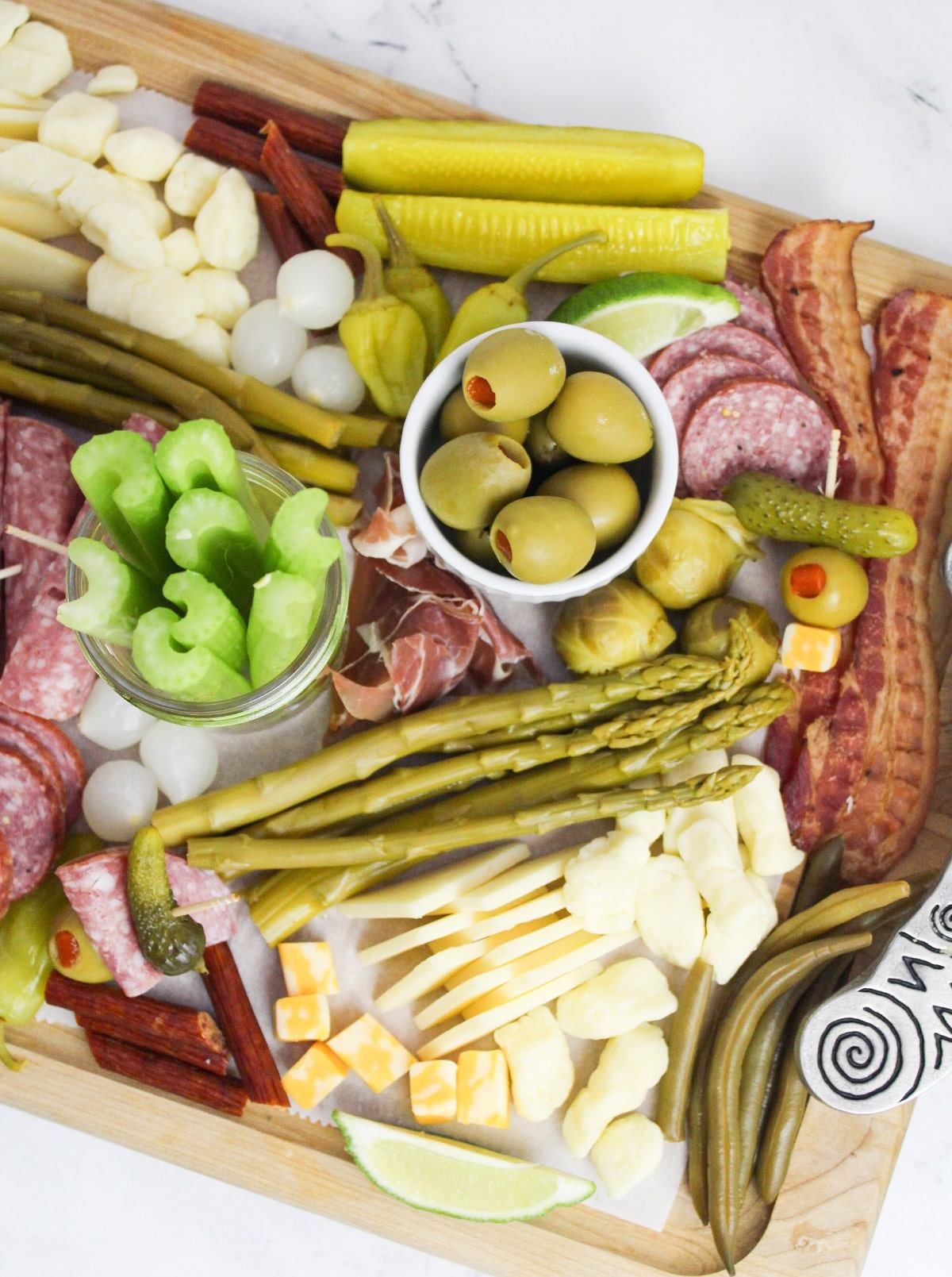 Overhead view of a completed board. The toppings are a variety of meats, cheeses, pickles, olives, pepper, vegetables.
