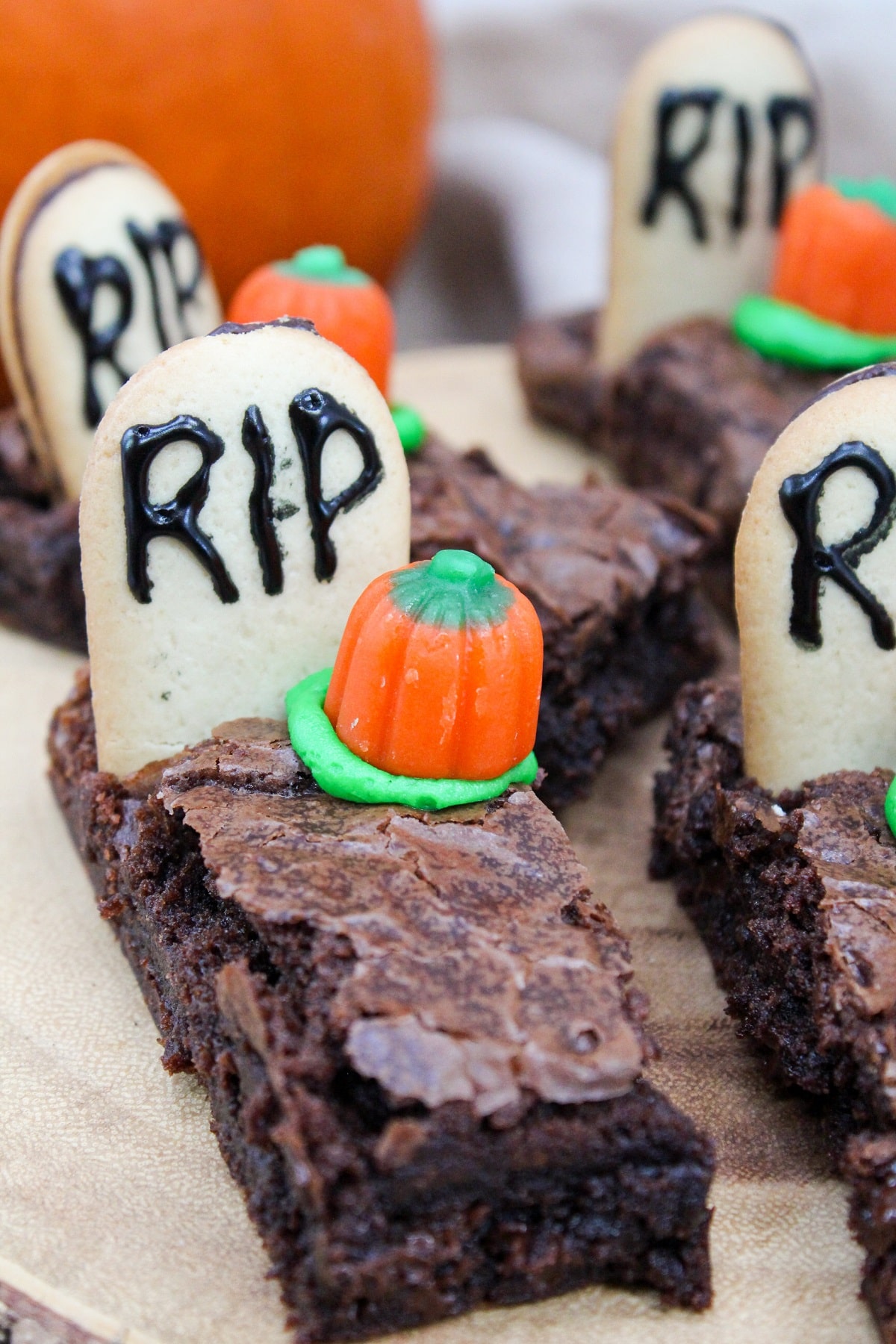 brownies cut into long pieces. Topped with a cookies with the letters RIP. A candy pumpkin and green frosting is next to the gravestone. 
