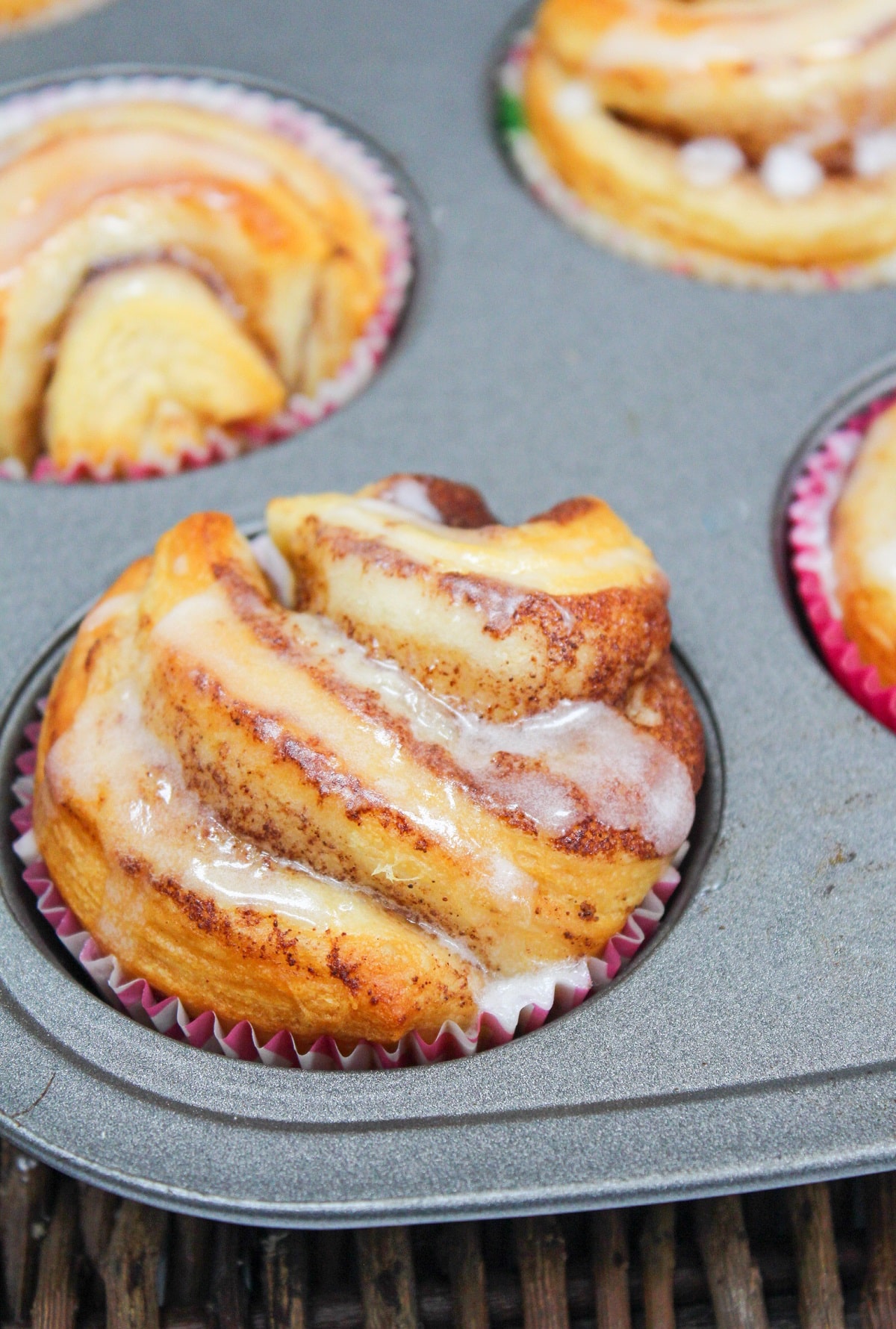individual cinnamon rolls in a muffin tin with a glaze on top.