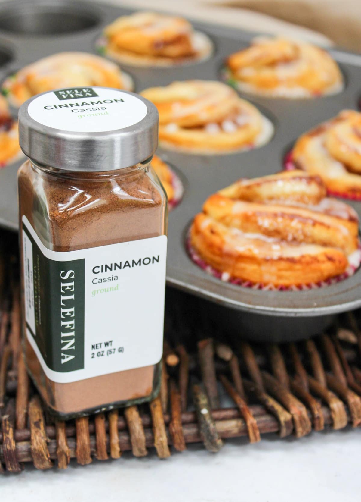bottle of ground cinnamon next to a pan of baked muffins.