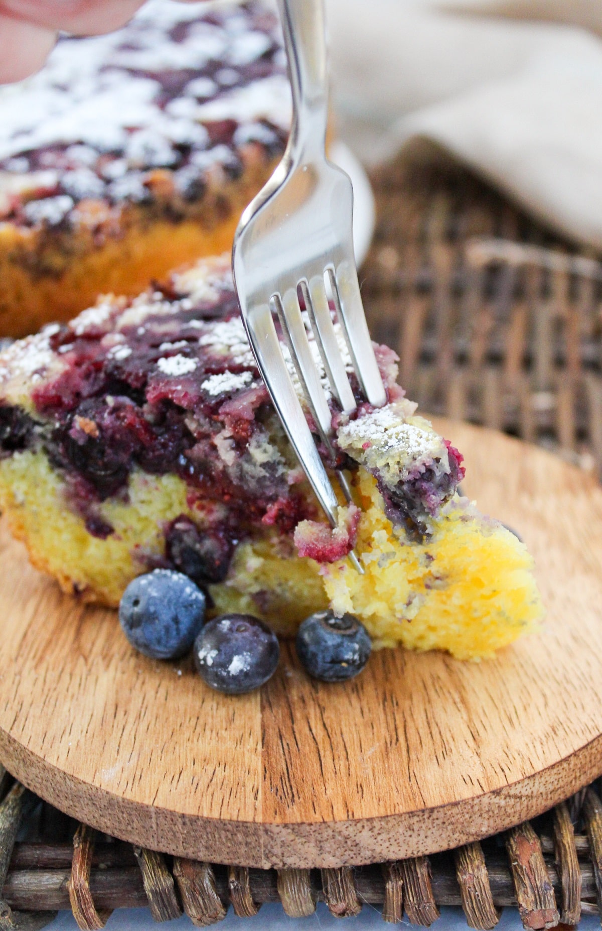 single slice of blueberry lemon cake with fresh blueberries on the side. A fork is in the cake to take a bite.