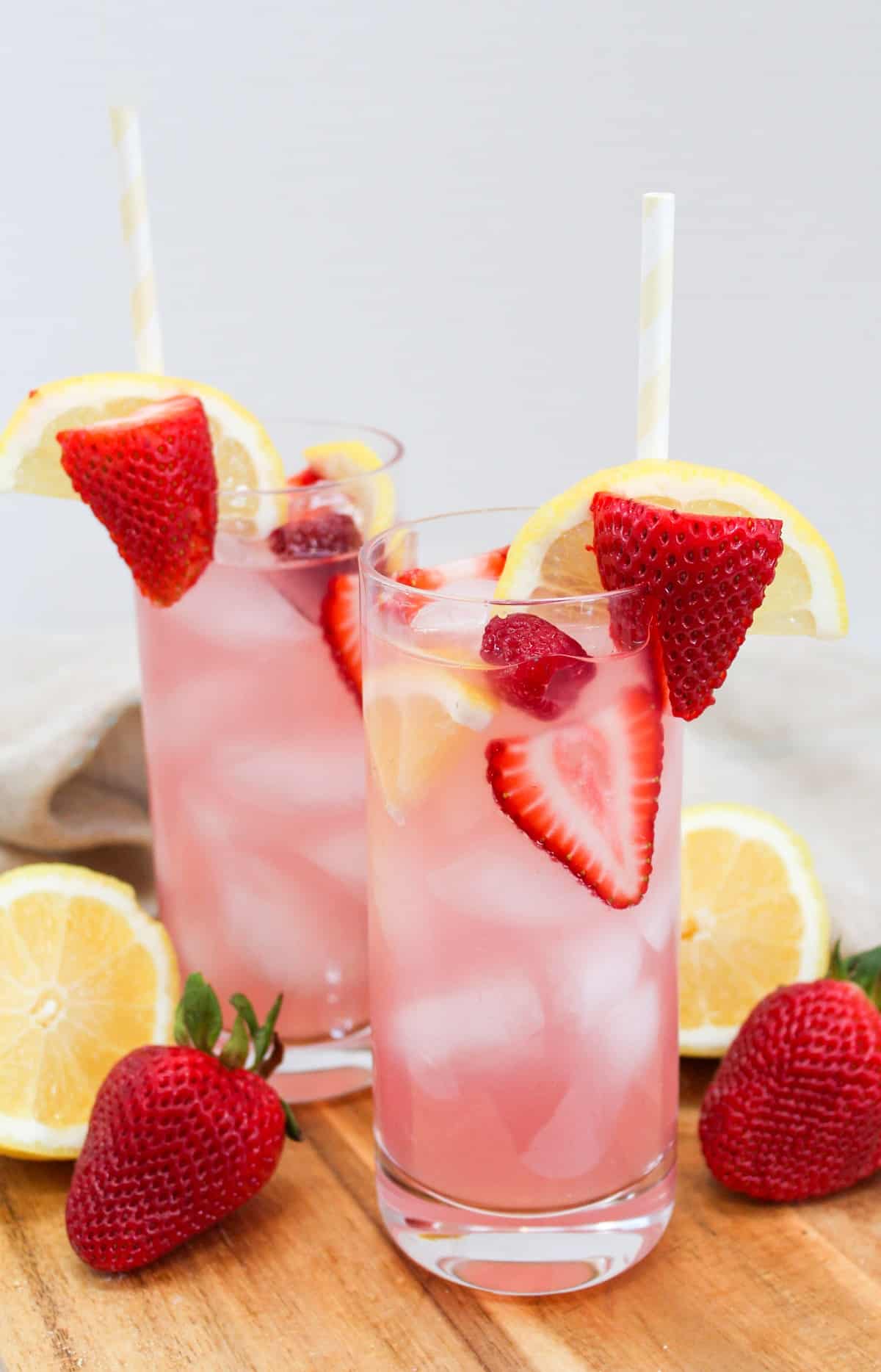 pink lemonade sangria in a tall glass garnished with strawberries, raspberries, and lemons.