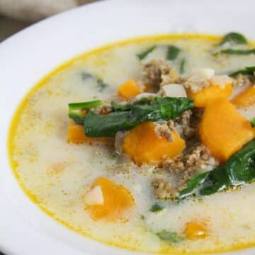 soup filled with sweet potatoes, ground sausage, and spinach in a white bowl.
