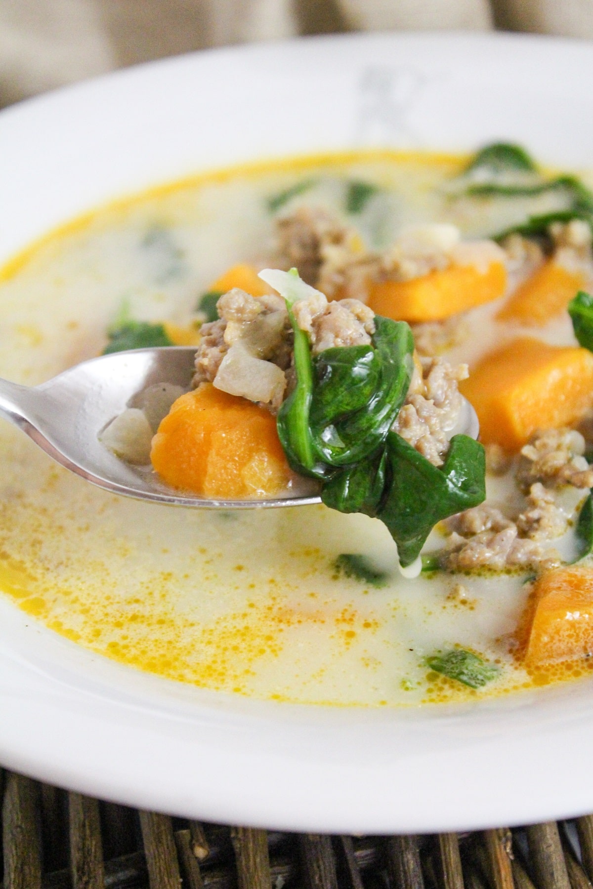 soup filled with sweet potatoes, ground sausage, and spinach with a spoon in a white bowl.