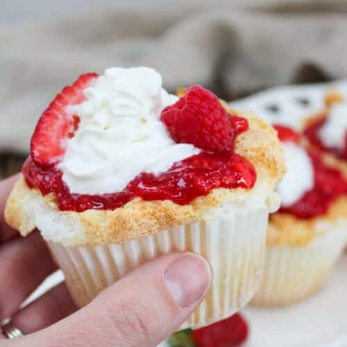 cupcake with berries and whipped cream on top held in hand.